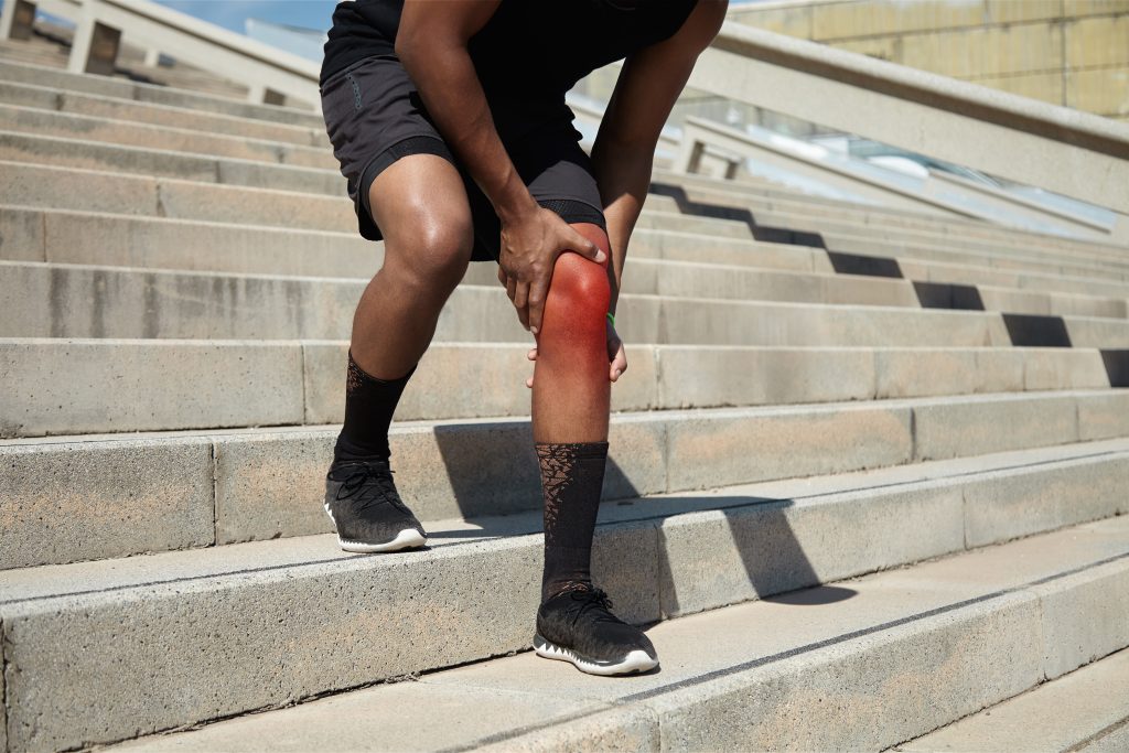 Man exercising on stairs has injured his knee and it is red and swollen