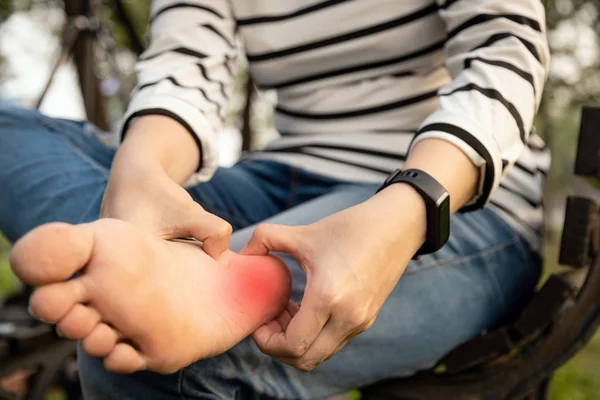 Person stopped on park bench bench. Holding foot due to pain caused by Jogger's Heel.